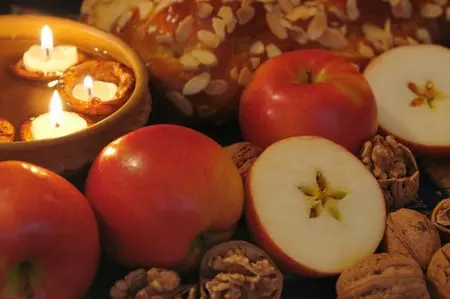 Rozkrojené červené jablko s jádrem a ořechy na tmavém pozadí.