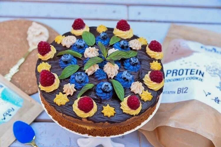 Vegan dort s ovocím a čokoládovou omáčkou na bílém podstavci.