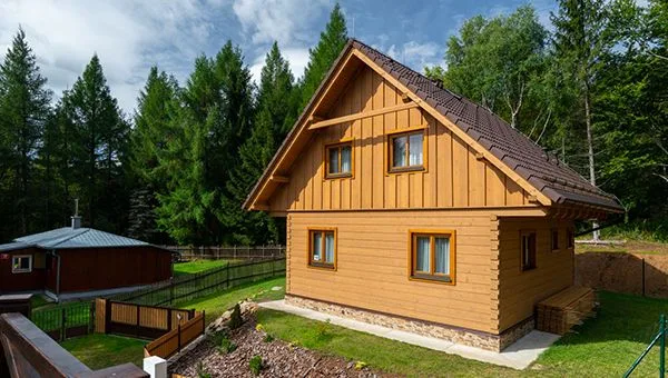 Malá dřevěná roubenka v přírodě s okny a střechou.