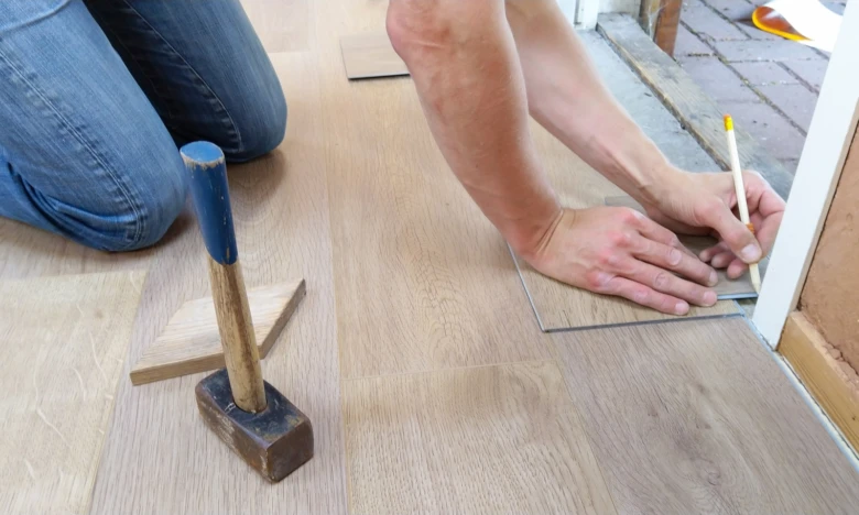Muž měří dřevěnou podlahovou desku při vyrovnávání.