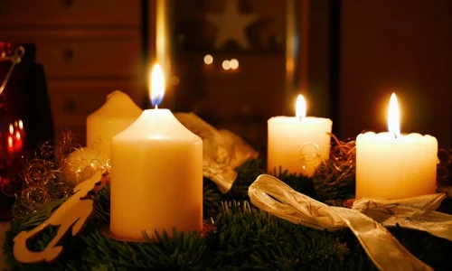 Zapálené adventní svíčky na zeleném věnci s ozdobami.