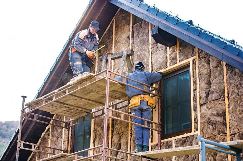 Pracovníci montují vnější tepelnou izolaci na dřevěnou chatu
