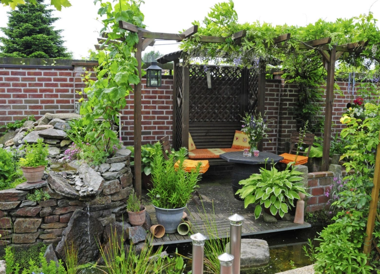 Zastíněná dřevěná pergola s rostlinami v zahradním sedacím koutku.