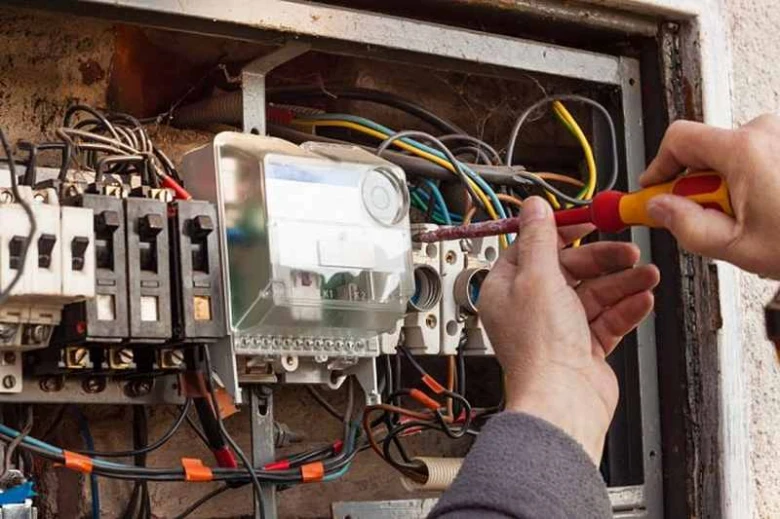 Elektrikář upravuje vodiče v rozvaděči šroubovákem.