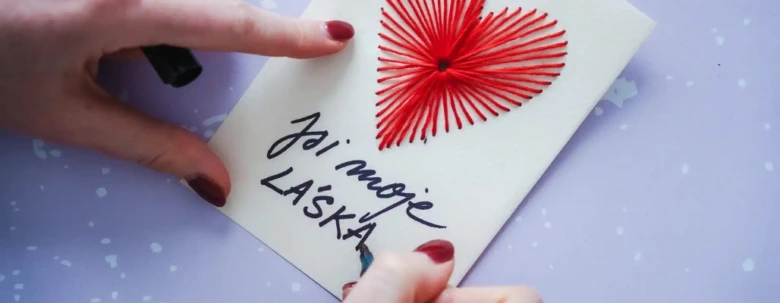 Rukou držená valentýnská kartička s červeným srdcem z nití.