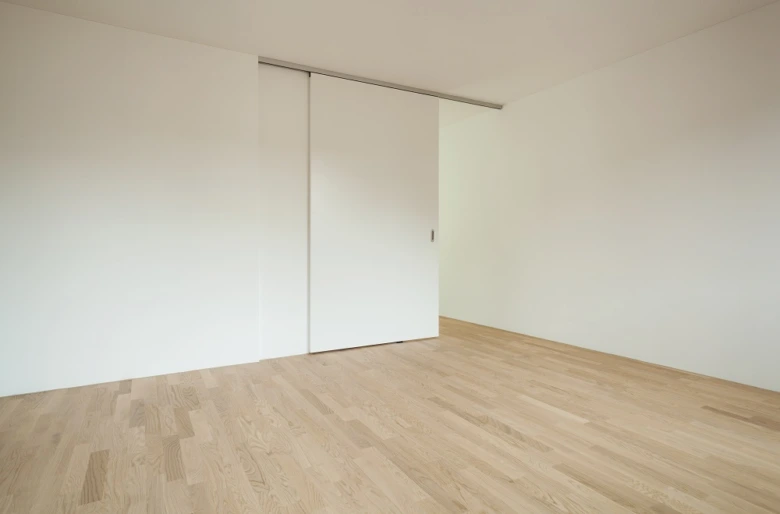 Bílé posuvné dveře skříně v moderním interiéru s dřevěnou podlahou.