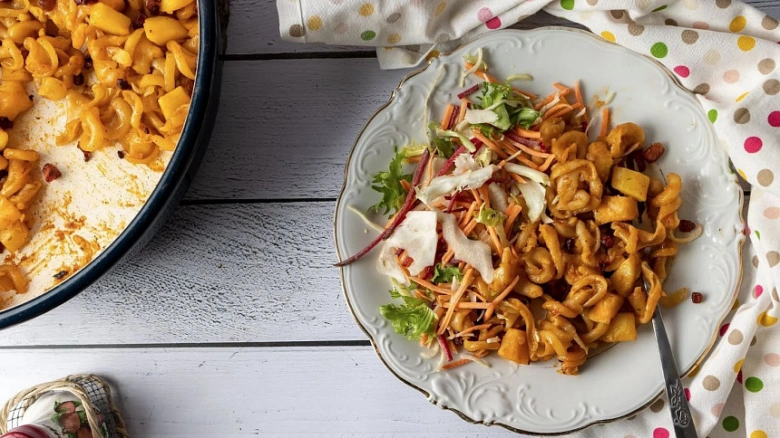 Pasta s salátem z mrkve na talíři vedle pekáče.