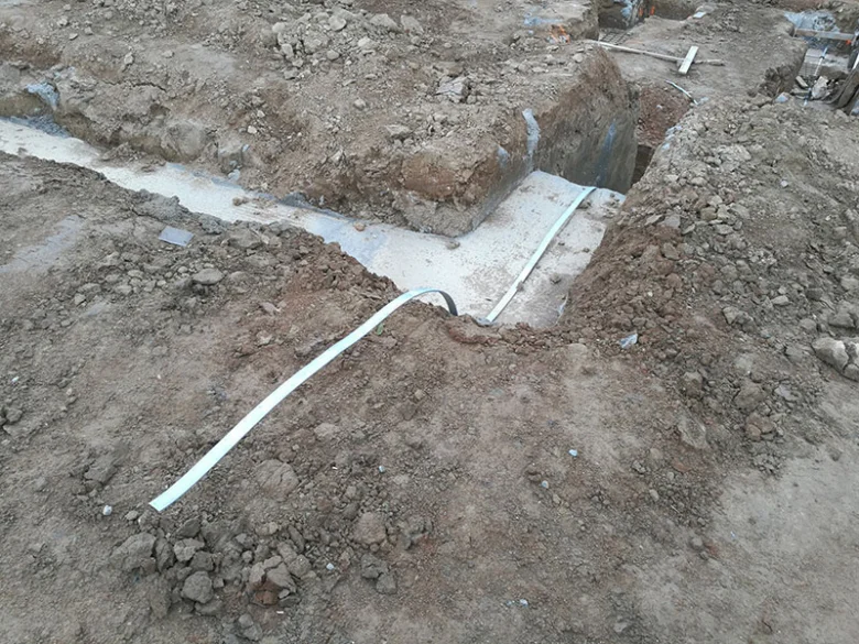 Bílý vodič uzemnění uložený v vykopaném příkopy pro elektrickou instalaci.