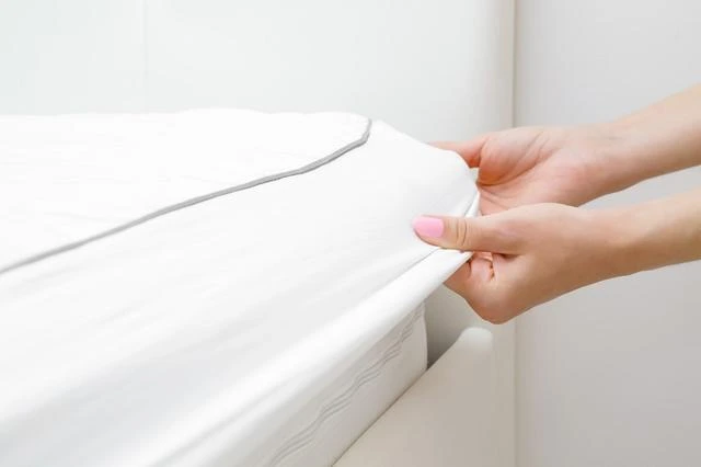 Ruční nasazování bílého prostěradla na matraci pro péči o ni.