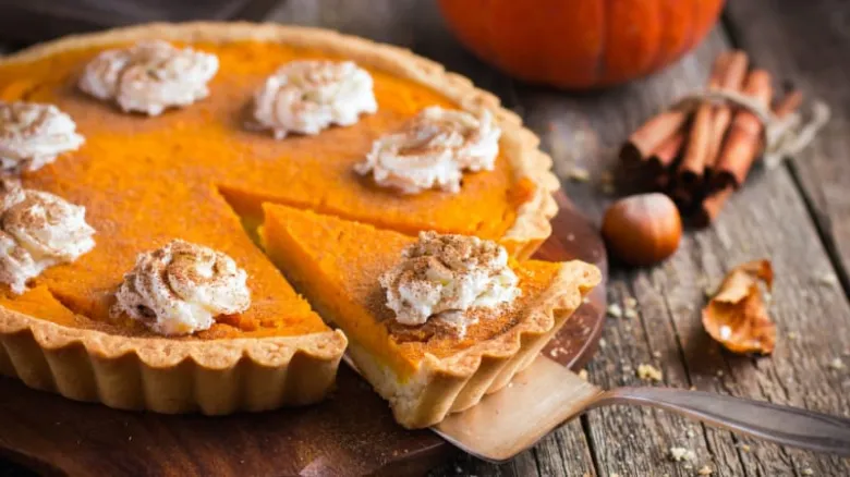 Pumpkinový koláč s bílou smetanou na dřevěném podkladu.
