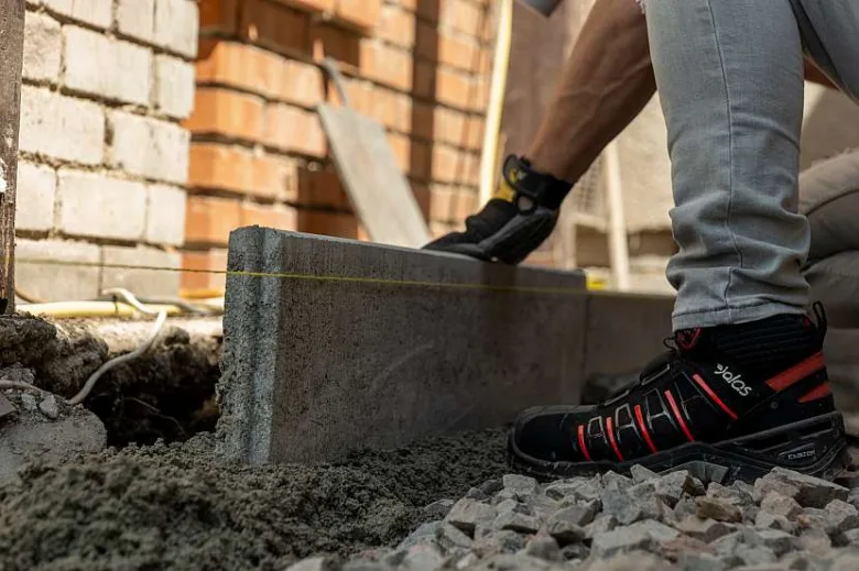 Stavebník položí betonový blok na štěrk pro chodník.