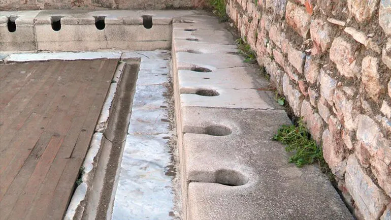 Řada tureckých záchodů s otvory v betonu vedle kamenné zeď.