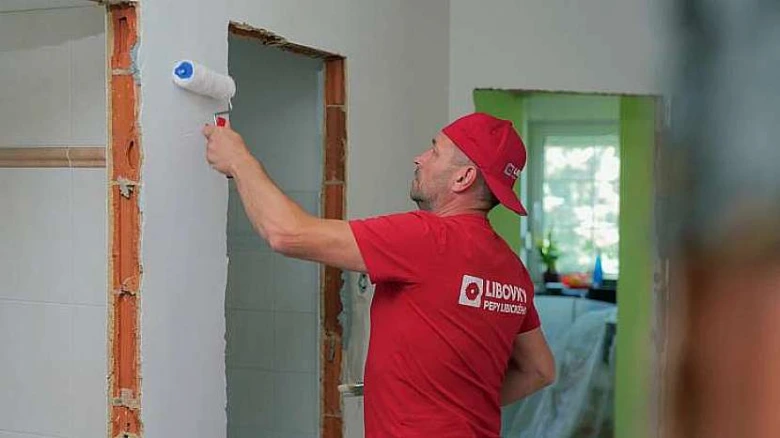 Muž maluje stěnu v bytě během rekonstrukce.