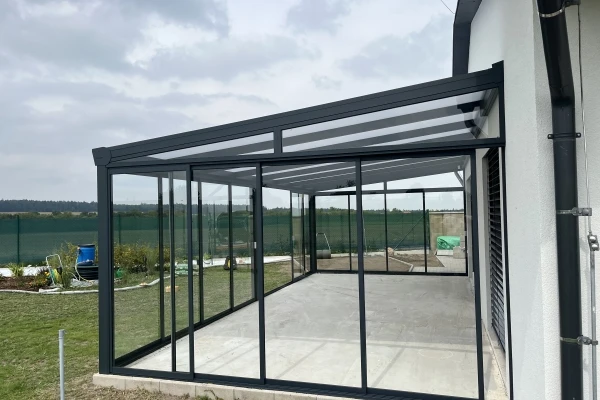 Dokončená zasklená pergola s černými rámy a skleněnými stěnami