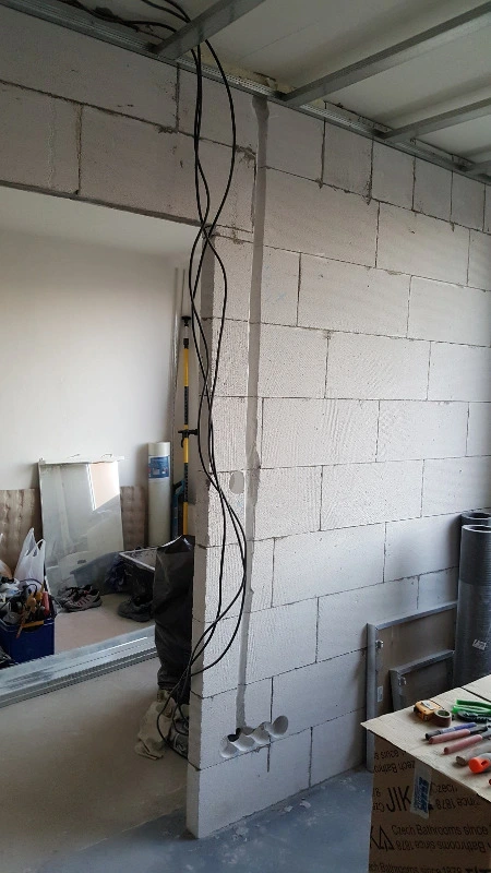Černé elektrické kabely vedoucí po zdivu během stavebních prací.
