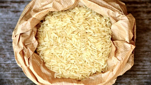 Nevysvařené rýže v hnědém papírovém sáčku na dřevěném povrchu.