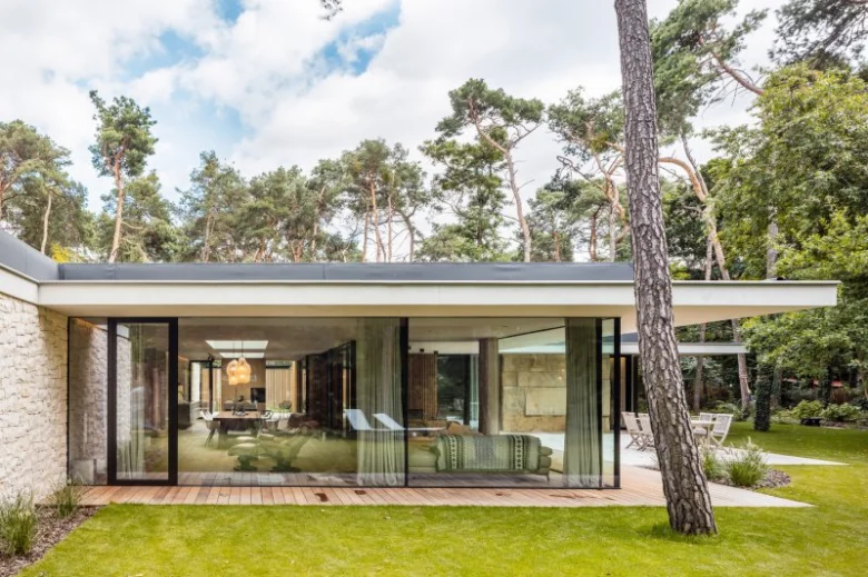 Moderní bungalov s velkými okny v přírodě mezi borovicemi.