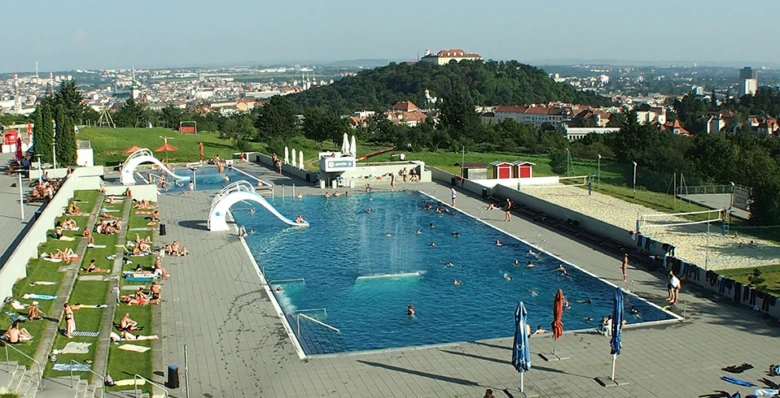 Venkovní plavecký areál s bazénem na kopci nad městem.