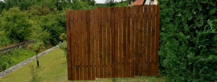 Dřevěný plot z panelů postavený svépomocí na trávníku.