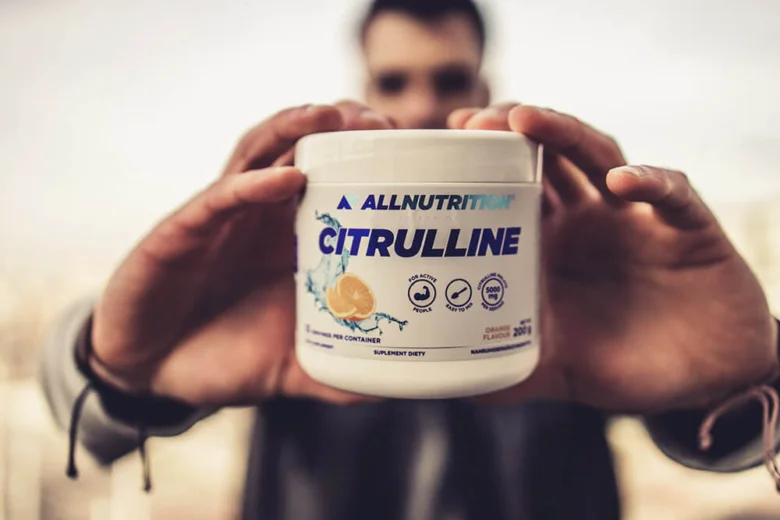 Bílá nádoba s citrulinem značky AllNutrition držená v rukou.