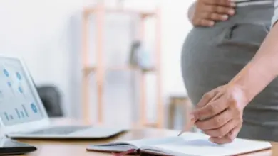 Těhotná žena píše u počítače při plánování peněžité pomoci v mateřství.