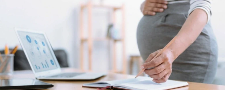 Těhotná žena píše u počítače při plánování peněžité pomoci v mateřství.