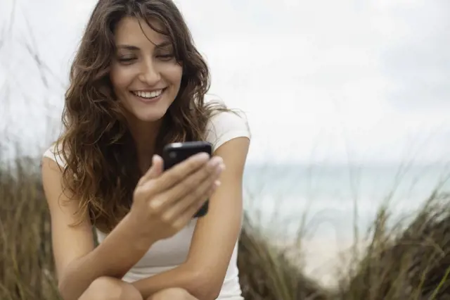 Žena se usmívá při používání mobilního telefonu venku.
