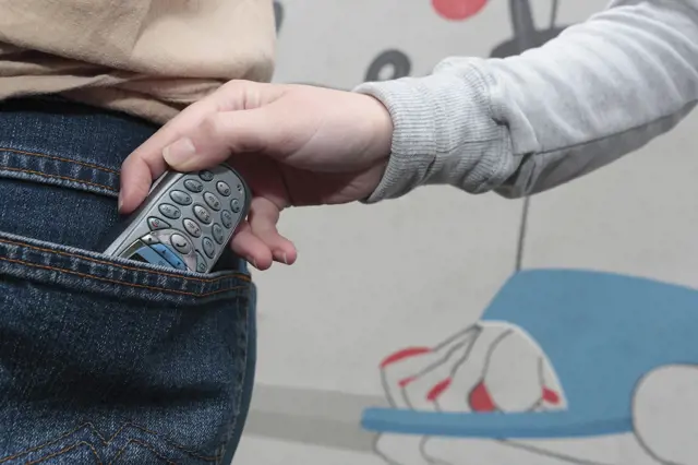 Ruka s mobilním telefonem v džínových kapsách.