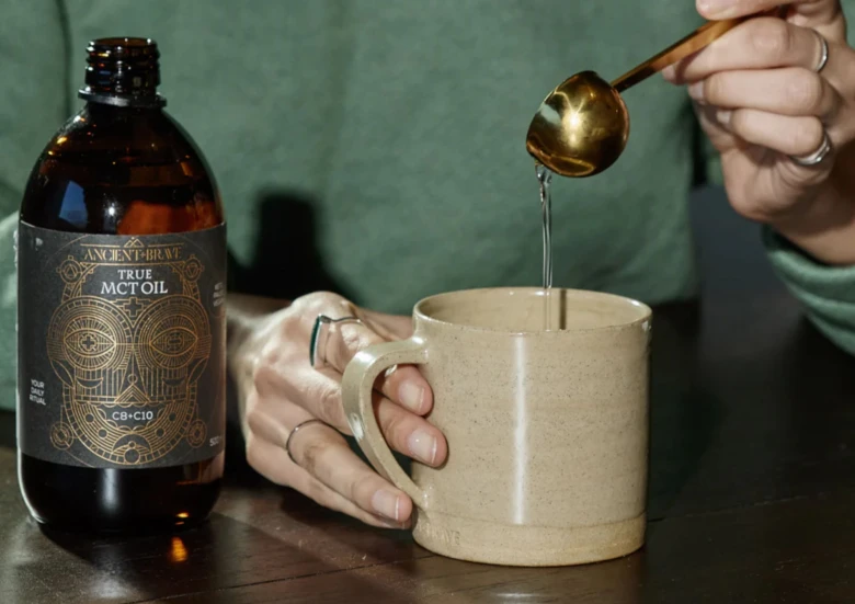 Lidé nalévají mct olej do šálku vedle lahve Ancient Brew.