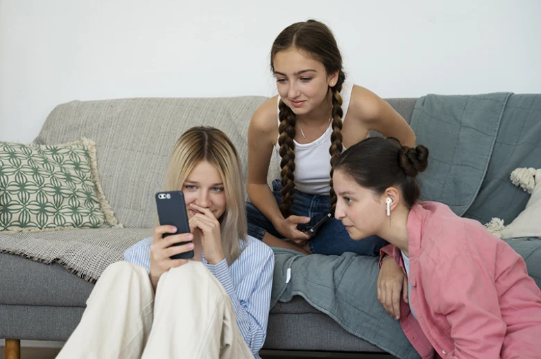 Tři dívky sedí na gauči a dívají se do telefonů.