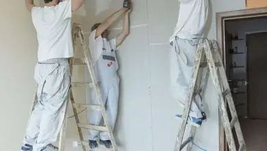 Tři dělníci montují sádrokartonový podhled na kovové nosiče.