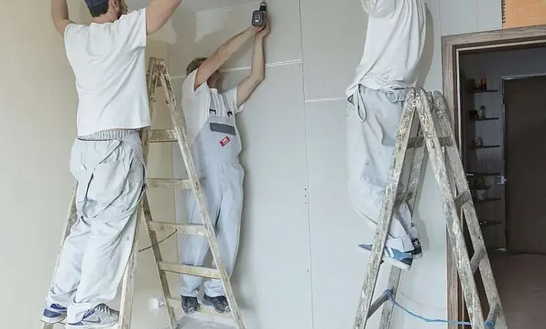 Tři dělníci montují sádrokartonový podhled na kovové nosiče.