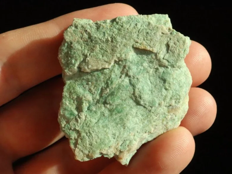 Ruka drží kus zeleného minerálu mastek s přírodní texturou.