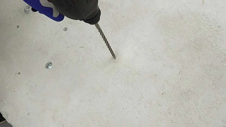 Ruční vrták se šroubovým bity vrtá do betonu.