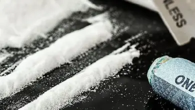Bílé práškové linie drogy na černém povrchu s nůžkami.