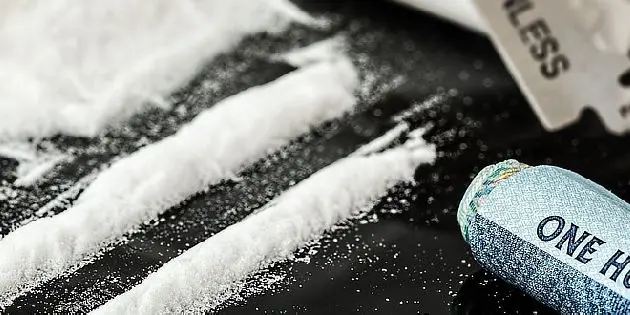 Bílé práškové linie drogy na černém povrchu s nůžkami.